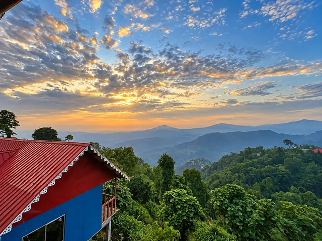 Red rooftops and green trees overlooking distant hills beneath a glowing evening sky