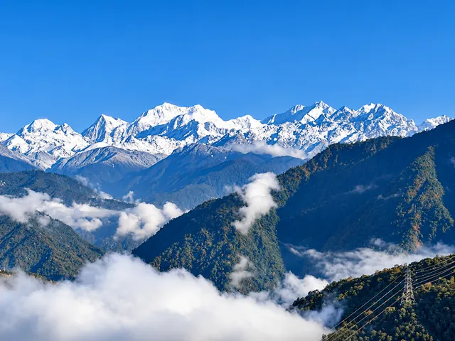 Snow-covered peaks rising above forested ridges and low clouds